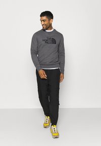 Felpa grigia con logo nero, pantaloni neri e sneakers gialle. Tessuto liscio sulla felpa, e vestibilità casual in tutto.