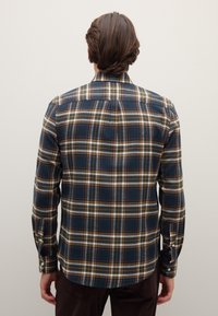 Camicia a quadri blu scuro, con linee gialle, bianche e rosse. Materiale in cotone, polsini con bottoni e design con orlo curvo.