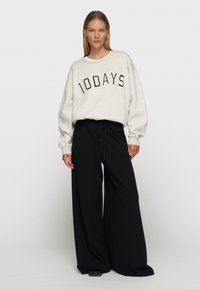 Sudadera gris claro con "10DAYS" impreso en negro. Combinada con pantalones negros de corte holgado. La tela parece suave y cómoda.