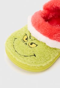 Zaļi samtaini čības ar smaidīgu Grinča seju, dzeltenām izšūtām acīm un spilgti sarkanu pūkainu apkakli. Mīksta tekstūra un noapaļota forma.