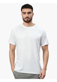 T-shirt bianca a maniche corte realizzata in tessuto leggero, con scollatura rotonda e superficie liscia, abbinata a pantaloni sportivi grigi.