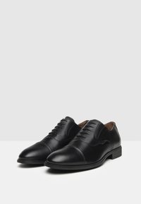 Chaussures habillées en cuir noir avec une finition lisse, bout rond, design à lacets et des détails de couture subtils sur les côtés. Semelle plate.