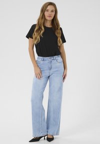 Ljusblå hög midja jeans med vida ben, tillsammans med en svart t-shirt med korta ärmar och svarta spetsiga klackar. Smidig denimtextur.
