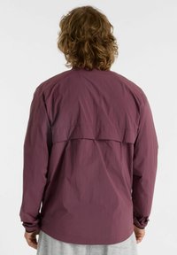 Long-sleeve shirt in dark burgundy fabric, featuring a back yoke detail, relaxed fit, and cuffed sleeves. Smooth, lightweight texture.
