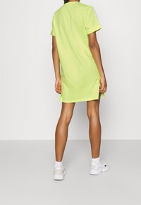 Neongrön kortärmad klänning med sidoklyftor, tillverkad av mjukt tyg, med rak skärning och minimalistisk design. Vita sneakers synliga.