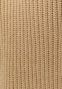 Tessuto a maglia di colore beige con una texture a coste verticale. Il materiale appare morbido con cuciture visibili in tutto il tessuto.