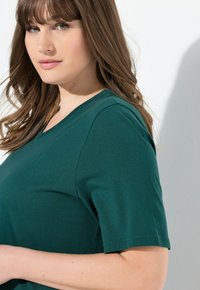 Zelené tričko s krátkým rukávem a výstřihem do V vyrobené z měkké bavlny. Má volný střih a čisté švy podél švů.