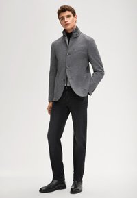 Szary, fakturowany żakiet z wysokim kołnierzem i zapięciem na guziki, zestawiony z ciemnymi dżinsami i czarnymi botkami za kostkę. Widoczne dwa przednie kieszenie.