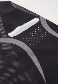 Černá sportovní tkanina s geometrickými šedými vzory, perforovanými detaily a výřezem v horní části pro ventilaci.