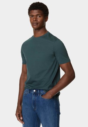 Dunkelblaugrünes T-Shirt mit kurzen Ärmeln aus glattem Baumwollmaterial, kombiniert mit blauen Jeans. Mit Rundhalsausschnitt und entspannter Passform.