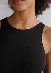 Top sin mangas ajustado y negro con un diseño de escote redondo. Textura suave y costuras mínimas, resaltando las líneas limpias de la prenda.
