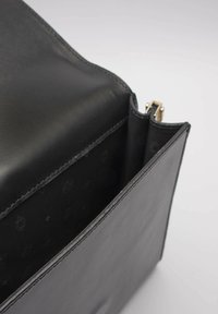 Czarna skórzana torebka o gładkiej fakturze, z otwartym wierzchem i złotym zamkiem błyskawicznym. Wnętrze wykończone czarną podszewką z subtelnym geometrycznym wzorem.