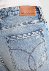 Jeans de mezclilla azul claro con un parche de cuero de Calvin Klein Jeans, que presentan acentos desgastados, costuras en contraste y un diseño tradicional de cinco bolsillos.