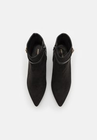 Botas de tobillo de ante negro con punta afilada y un tacón bajo, que cuentan con una correa decorativa y un detalle de cremallera en el lateral.