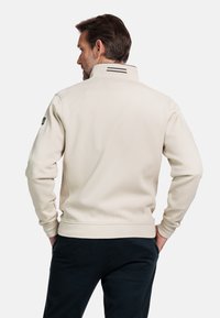 Beige sweatshirt voor heren met een hoge kraag, ribgebreide manchetten en een rugpanddetail. Voorzien van zijzakken en een stoffen logo-opdruk op de mouw.