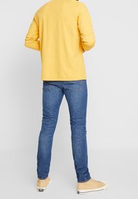 Långärmad gul bomullsskjorta, blå slim-fit jeans och beige sneakers. Enkelt mönster, enfärgad och avslappnad passform.