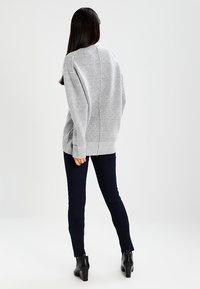 Jersey gris de punto con un corte relajado, que presenta un cuello alto y puños acanalados, combinado con jeans skinny oscuros y botas de tobillo.