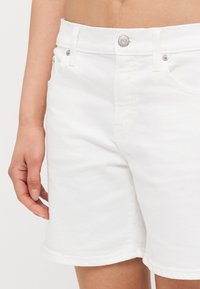 Pantalones cortos de mezclilla blanca con un diseño ajustado, estilo de cinco bolsillos y cierre de botón metálico. Presenta dobladillo enrollado y sutiles detalles de costura.