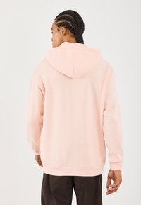 Felpa rosa chiaro con cappuccio, maniche lunghe, realizzata in morbido materiale misto cotone e dal taglio rilassato. L'orlo inferiore e i polsini sono a costine.