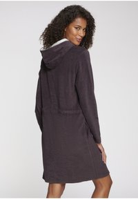 Temno vijolična kopalna halja s kapuco, teksturirano blago, stranskimi žepi in prilegajočim pasom. Notranjost ima svetlejšo podlogo in detajle na manšetah.