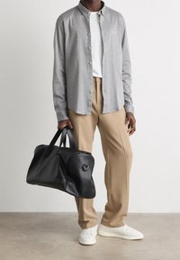 Grijze lange mouwen shirt, witte t-shirt, beige broeken, zwarte leren sporttas en witte sneakers. Opmerkelijke knoopdetail op het shirt.