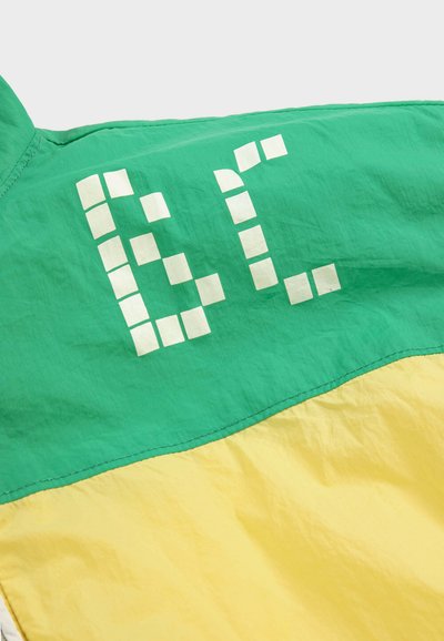 Tissu vert et jaune avec des lettres pixellisées blanches "6L" imprimées sur la section verte, montrant la texture du tissu et les détails de la couture.