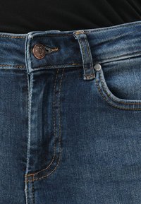 Dark blue denim jeans with copper button, contrast stitching, side pocket, faded texture in areas, and standard jean design details.