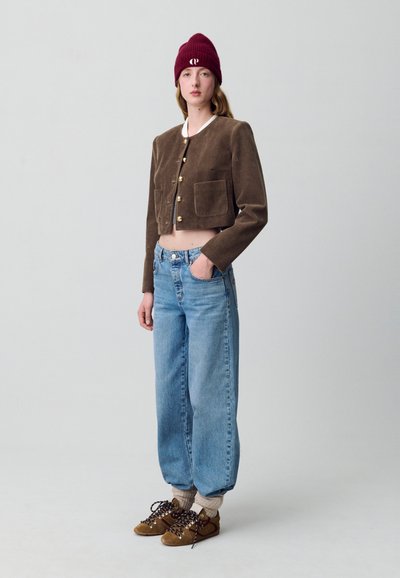 Giacca cropped in corduroy marrone con bottoni dorati, jeans a vita alta blu, calzini alla caviglia beige e scarpe marroni con lacci. Berretto bordeaux.