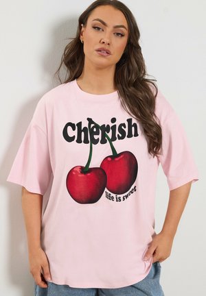 Frau mit langen braunen Haaren trägt ein hellrosa T-Shirt mit zwei großen Kirschen und dem Text „Cherish life is sweet.“