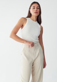 White ribbed tank top paired with high-waisted beige wide-leg trousers, featuring a smooth texture and side pockets.