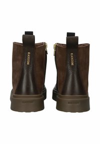 Hnědé nubukové kotníkové boty s kontrastními koženými akcenty, vybavené bočním zipem, textilním poutkem a gumovou podešví s embosovaným brandingem.