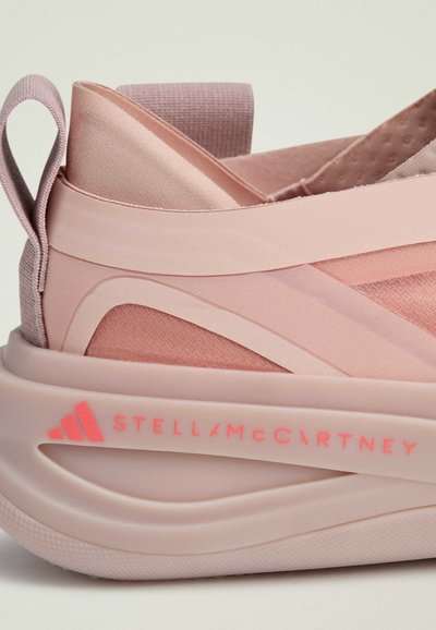 Pink athletic shoe with layered materials, elastic straps, a textured upper, and a thick sole featuring a logo in bright pink.