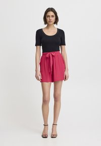 Haut noir à manches courtes associé à un short taille haute rose avec une ceinture à nouer. Tissu doux et coupe décontractée. Design simple et moderne.