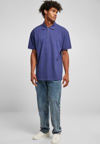 Polo shirt violet avec un col boutonné, associé à un jean bleu délavé et des baskets blanches. Manches courtes et design décontracté.