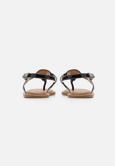 Svarta lackläderssandaler med platt sula, justerbara ankelremmar och bruna fotsängar, som visar en minimalistisk design.
