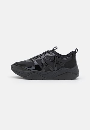 Zapatilla negra con texturas mixtas mate y brillantes, suela gruesa, diseño con cordones y lengüetas de tela en el talón y la lengüeta.
