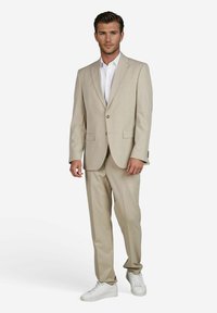Beige pak gemaakt van lichte stof, met een enkelxuitsluiting blazer met twee knopen, in combinatie met bijpassende broek en witte sneakers.