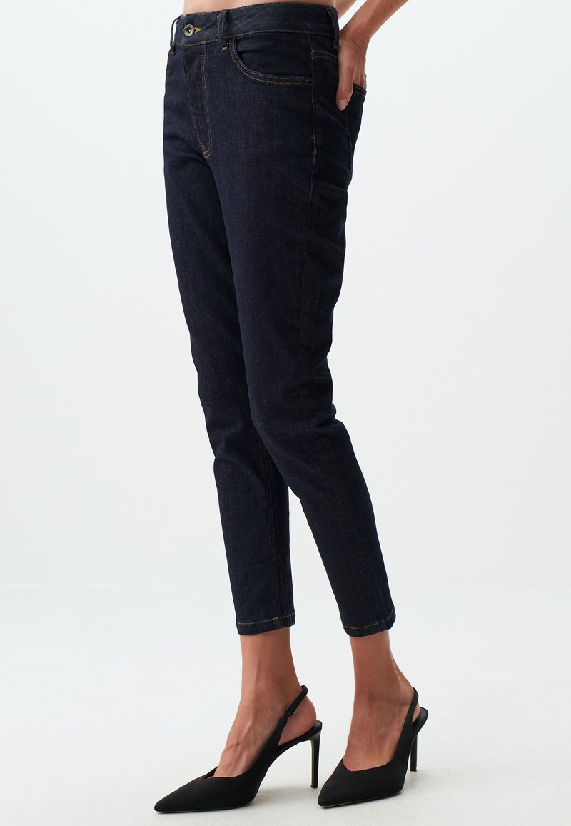 Jeans in denim scuro con vestibilità slim e lunghezza cropped. Presentano cuciture dorate, cinque tasche e una chiusura con zip e bottone.