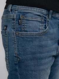 Vaqueros de mezclilla en un azul medio con costuras en naranja contrastante, que cuentan con un bolsillo para monedas y etiquetas de la marca en la parte delantera y trasera.