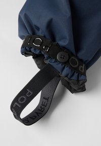 Mørkeblå stofmanchet med sort elastisk bånd og knap. Har et vævet bånd mærket "POLAR" og en struktureret yderside.