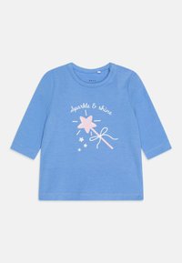 Camisa azul de manga larga hecha de algodón suave, con un estampado en blanco de "Brilla y Brilla" que presenta un diseño de estrella rosa y varita.