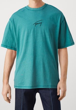 T-shirt en coton bleu sarcelle à coupe ample. Doté d'un col rond et du logo "Tommy" brodé en noir sur la poitrine gauche. Manches courtes et design simple.