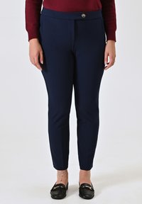 Pantaloni attillati blu navy con una texture liscia e chiusura con bottone in vita. Indossati con mocassini neri.
