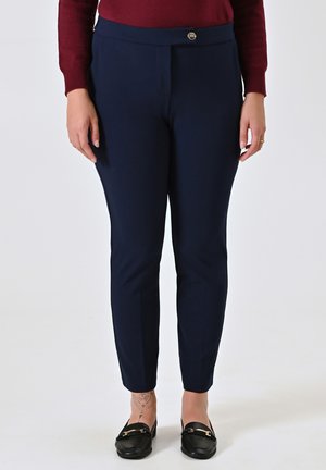 Pantaloni attillati blu navy con una texture liscia e chiusura con bottone in vita. Indossati con mocassini neri.