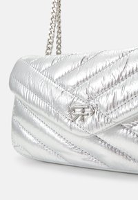 Metallisch silberne, gesteppte Handtasche mit Zickzackmuster, ausgestattet mit einem silbernen Kettenriemen und einem Logo-Details auf der Vorderseite.