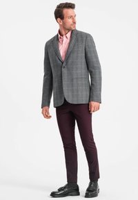 Blazer grigio a quadri con un singolo bottone, abbinato a una camicia rosa chiaro. Pantaloni bordeaux scuro e scarpe nere completano l'outfit.