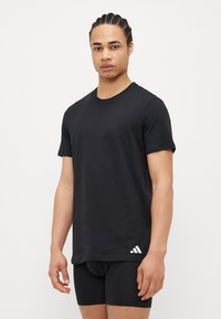 Fekete pamut póló kerek nyakkal és rövid ujjakkal, az alsó részen fehér Adidas logóval. Egyszerű, laza dizájn.