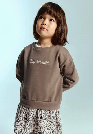 Sweatshirt marron avec broderie "Tiny but wild", associé à une jupe imprimé léopard. Présente un col rond et des manches longues.