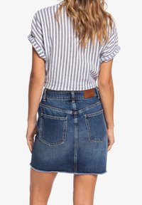 Jupe en denim avec un ourlet effiloché, de couleur bleu foncé, dotée de deux poches arrière et d'une étiquette en cuir marron à la taille, associée à un haut cropped rayé.
