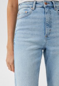 Vaqueros de mezclilla de color azul claro con cintura alta, que cuentan con un diseño de cinco bolsillos, herrajes de cobre y un ligero desgastado en la tela.